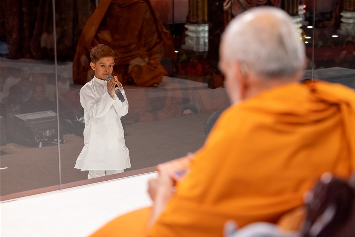 A child speaking into a microphone before Mahant Swami Maharaj